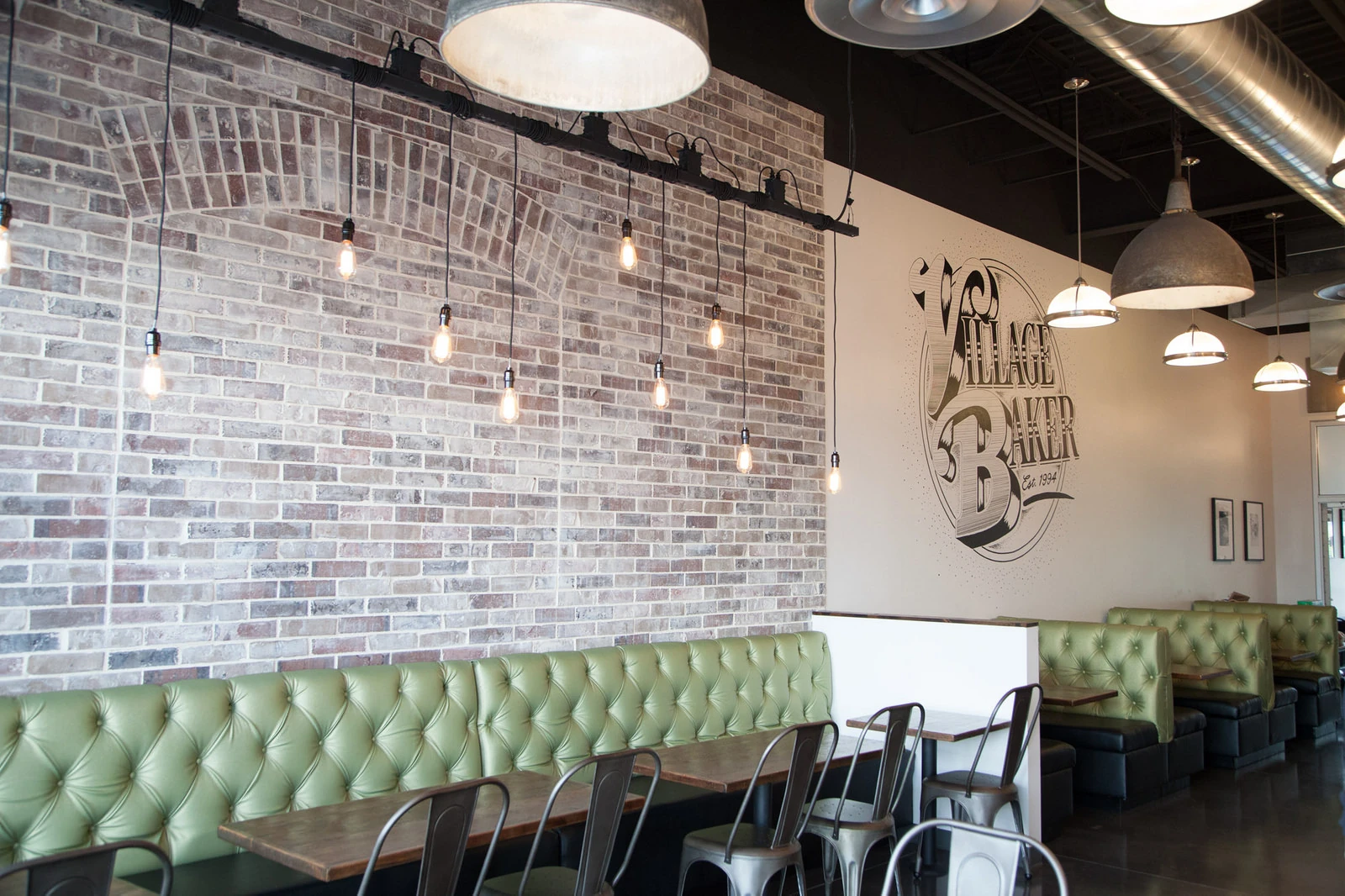 Village Baker dining room with mural, green booths, and industrial lighting